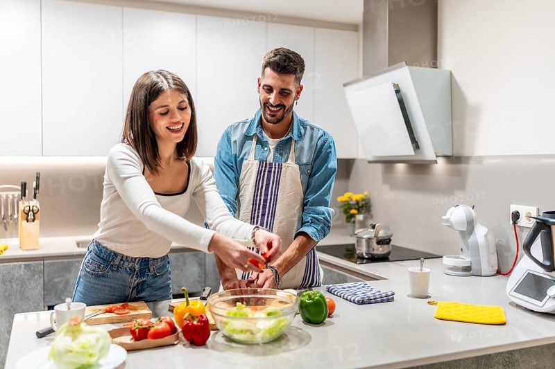 Young couple smiling and joyfully preparing a vibrant, healthy salad together in their modern kitchen, sharing moments of love and teamwork