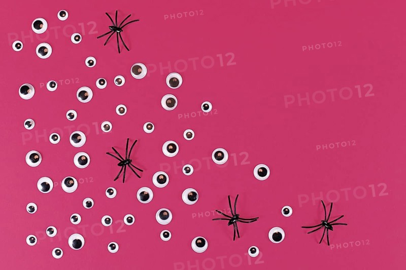 Halloween flat lay with lots of spooky googly eyes and plastic spiders on pink background with empty copy space