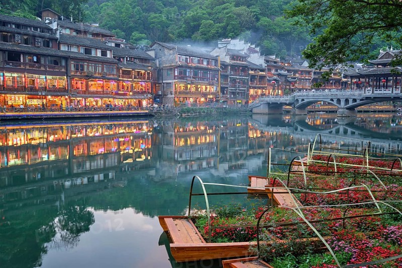 Chinese tourist attraction destination, Feng Huang Ancient Town (Phoenix Ancient Town) on Tuo Jiang River with bridge illuminated at night. Hunan Province, China, Asia