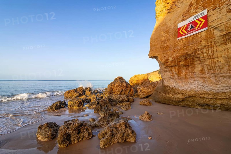 ROCKFALL UNSTABLE CLIFFS, KEEP A SAFE DISTANCE is written in English on a warning sign in Portugal on the cliffs of the Atlantic Ocean. Rocks and stones break out here again and again and injure people., Albufeira, Faro, Portugal, Europe