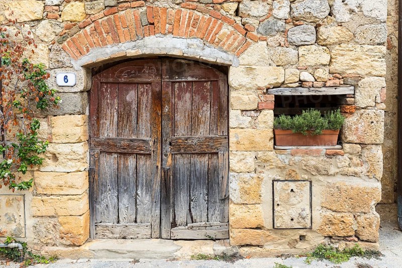 Quarry stone wall with old wooden door and house number 6, rosemary in a flower box, in the historic centre of Monteriggioni, province of Siena, Tuscany, Italy, Europe