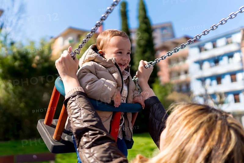 Happy little boy enjoying time on a swing while his mother lovingly pushes him in a vibrant playground, filled with laughter and joy