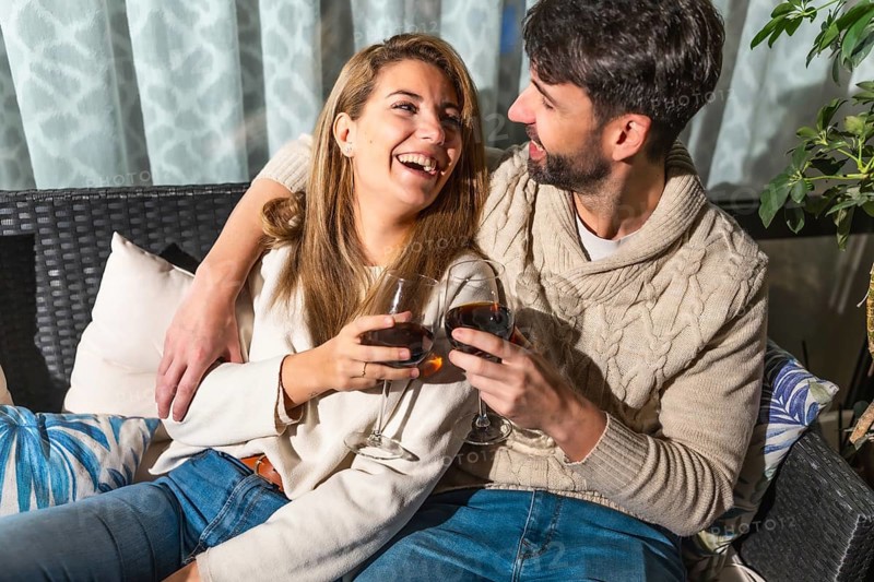 Romantic couple enjoying a relaxing evening together, sharing drinks and laughter on a comfortable sofa