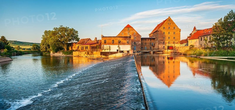 Historic watermill reflected in the river Unstrut with weir in the evening light, Laucha, Saxony-Anhalt, Germany, Europe
