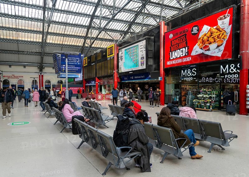 People sitting in seats in concourse area of Lime Street railway station, Liverpool, England, UK
