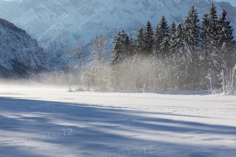 Misty morning on Lake Almsee which is frozen and snow covered. Snow on the forest with blue sky