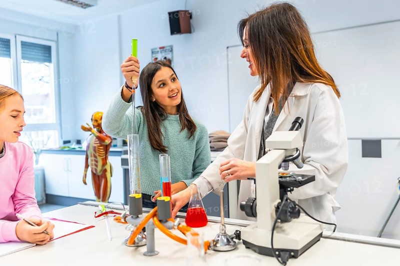 Female teacher assisting students during a chemistry experiment in a school laboratory, promoting stem education and scientific exploration