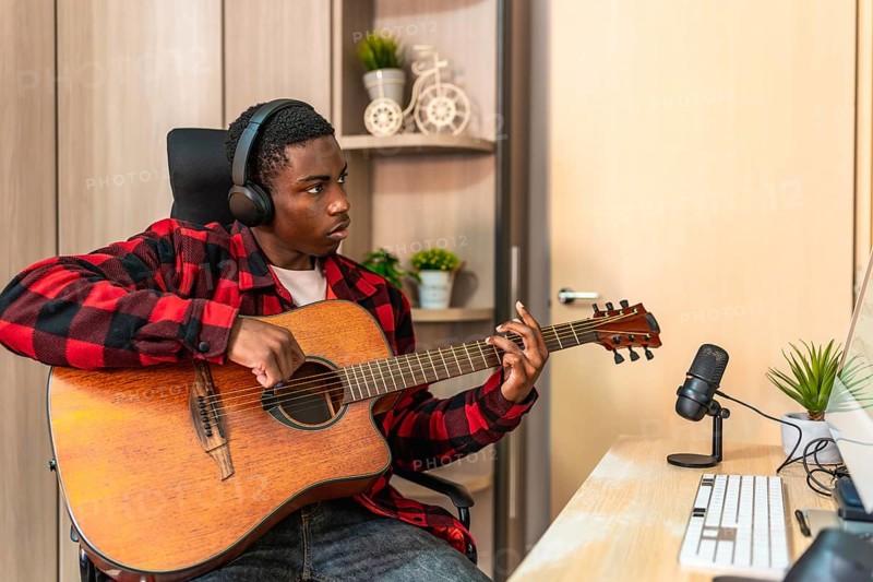 Concentrated young man playing the acoustic guitar in his home studio, composing a new song and recording with a microphone