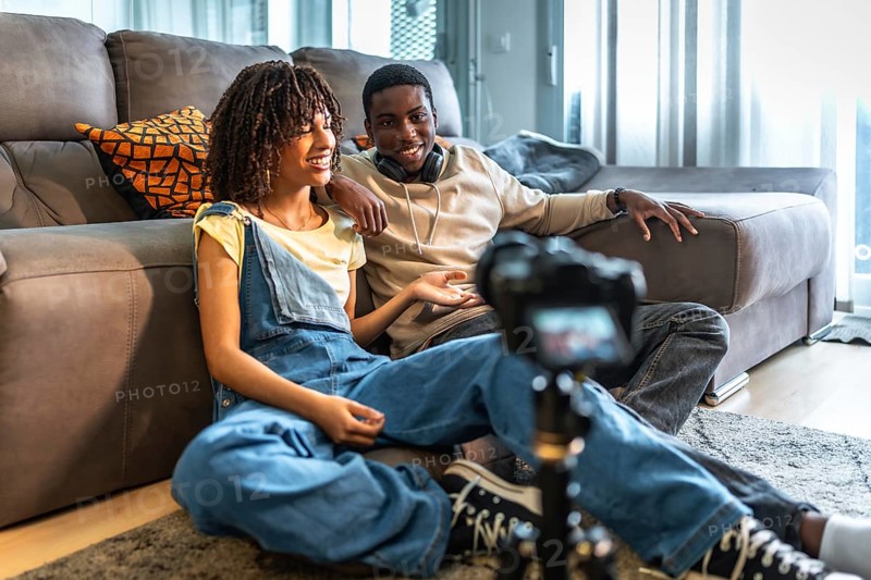 Two videomakers are creating content for their channel, discussing and smiling while recording a vlog in their living room