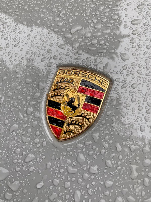 Porsche crest on grey bonnet of sports car with sparkling raindrops, international