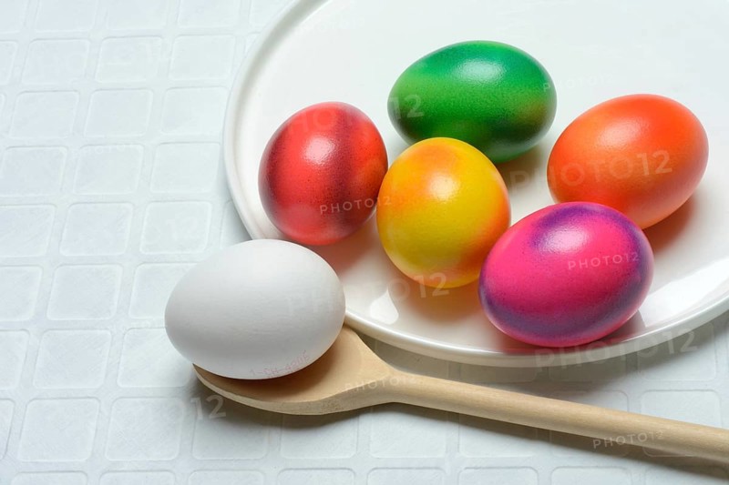 Coloured eggs on a plate and uncoloured eggs on a spoon, Easter celebration