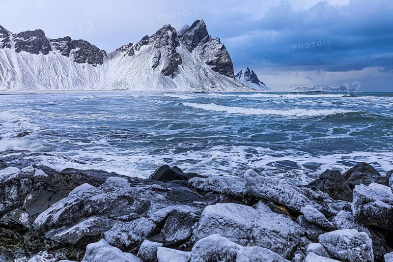 Iced rocks on the beach of Stokkness, behind them the snowy rocky slopes of Vestrahorn, near Höfn, Sudausturland, Iceland, Europe