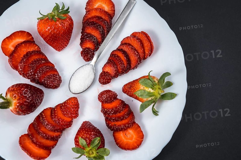 Natural strawberries on a white plate with a spoon of sugar with black background