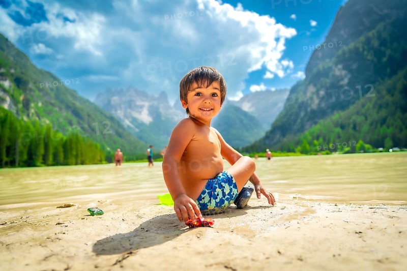 Smiling child playing with a toy car on the shore of lake landro, also called durrensee, in the italian dolomites, enjoying the summer holidays