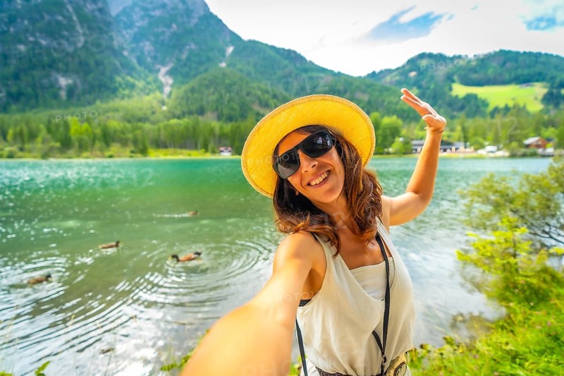 Happy tourist taking a selfie at lake dobbiaco with ducks swimming in the emerald green water and the dolomites in the background during summer holidays