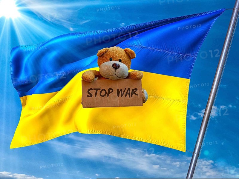 Symbolic picture, Ukraine flag in front of a bright sky, sad little bear with Stop War sign, Donald Trump wanted dictator, Republicans, Russia war against Ukraine, global danger, lies, 2nd term, global burden, questionable USA deal with Russia, scandal in the White House against President Volodymyr Selenskyj in front of running cameras