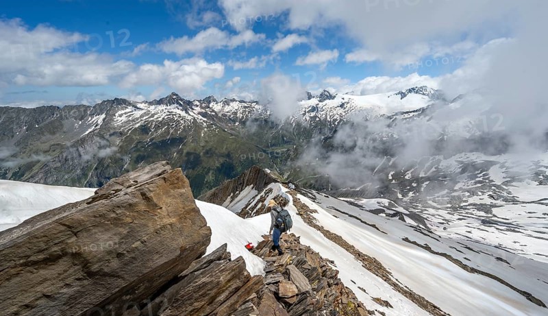 Mountaineer on a rocky ridge with snow, descent from the summit of Schönbichler Horn, view of snow-covered mountain peaks and valley Zemmgrund, Berliner Höhenweg, Zillertal Alps, Tyrol, Austria, Europe