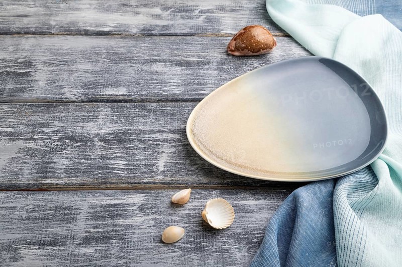 Empty blue ceramic plate on gray wooden background and blue textile. Side view, copy space