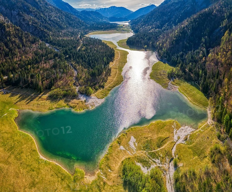 Green mountain landscape with river and lake, sun reflection in the water, surrounded by forests, Mittersee lake