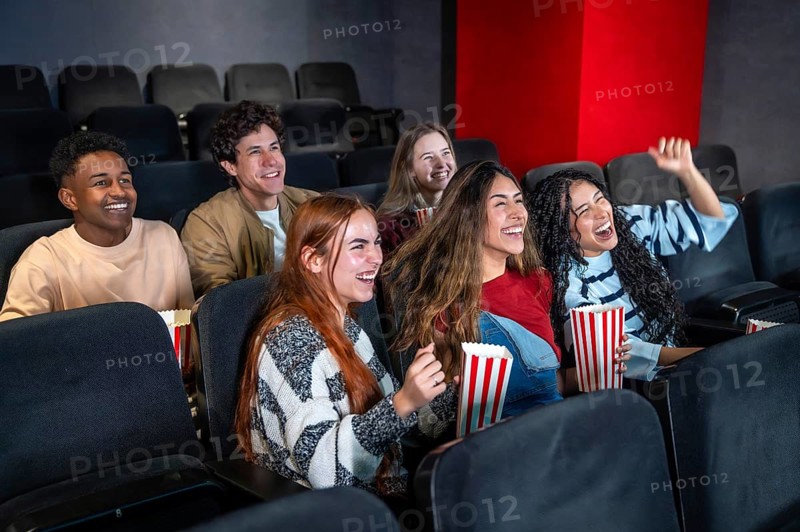 Young people having fun watching a film at the movie theater, eating popcorn and laughing