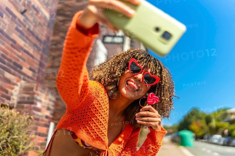 Young and vital latin woman taking selfie while eating lollipop outdoors