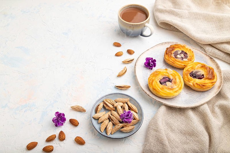 Small cheesecakes with jam and almonds with cup of coffee on a white concrete background and linen textile. Side view, copy space