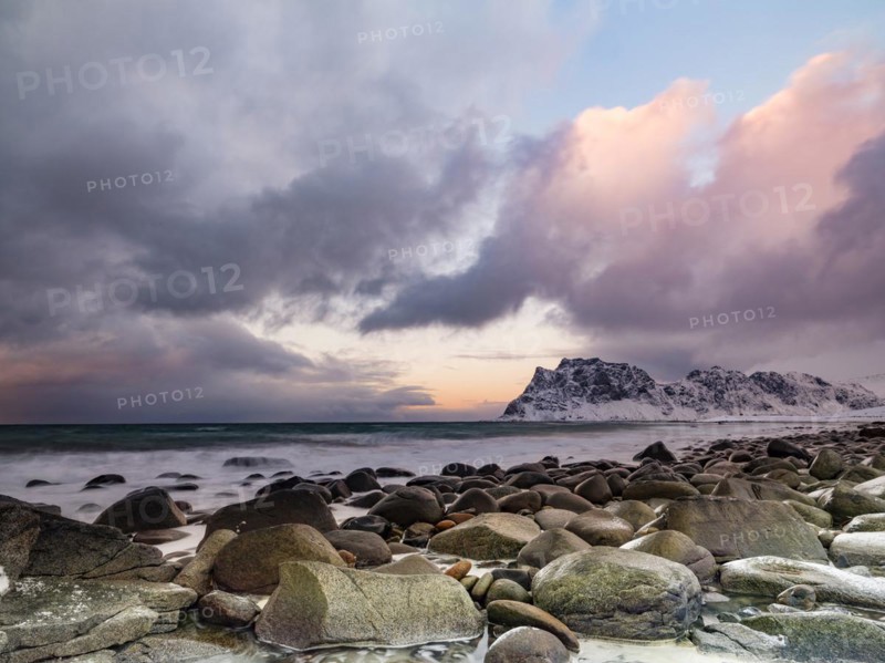 Rounded rocks on Utakleiv beach in a dramatic cloudy atmosphere, snow-capped mountains in the background, Vestvagoy Island, Lofoten, Norway, Europe