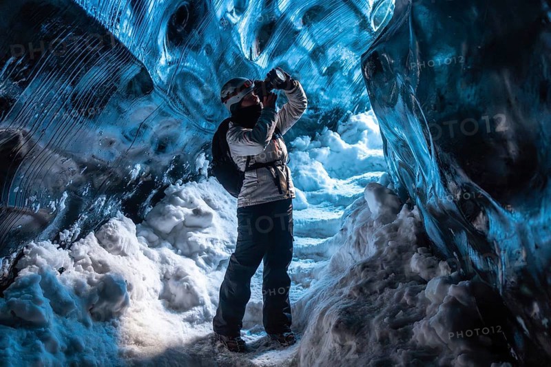 A woman is standing in a cave with snow on the ground. She is wearing a backpack and a white jacket