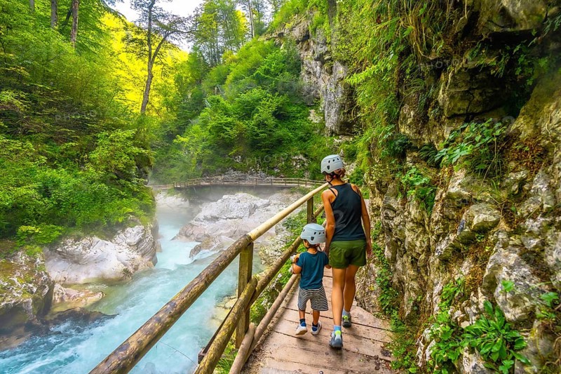 Mother and son wearing helmets walking on wooden path and enjoying breathtaking view of radovna river flowing through vintgar gorge in slovenia