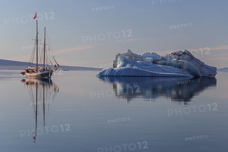 Traditional sailing ship reflected in fjord next to iceberg, sunny, Ittoqqortoormiit, Scoresby Sund, East Greenland, Greenland, North America