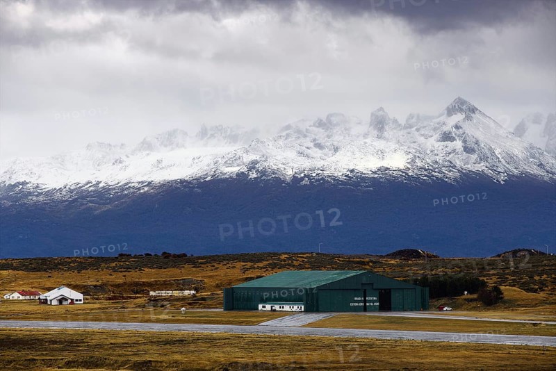 View from the deck of the cruise ship to an industrial hall in front of a snow-covered mountain range under a cloudy sky, Ushuaia, Argentina, South America