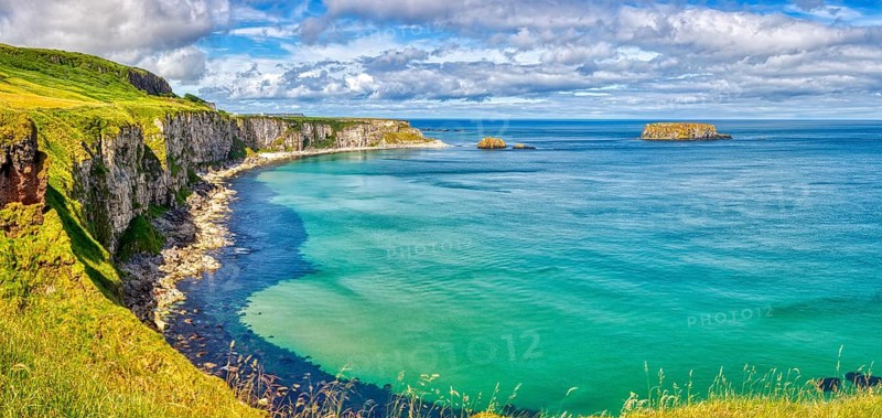 Vast coastal landscape with cliffs and bright blue sea under partly cloudy skies, County Antrim Coast