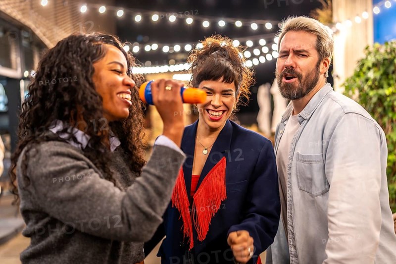 Latin woman singing karaoke next to friends at night party in the terrace of a bar