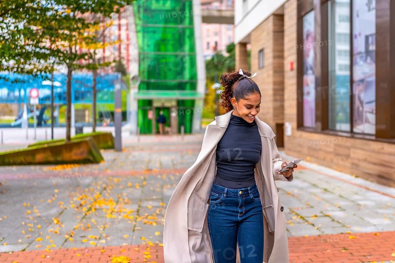 Happy young african american businesswoman using phone while walking on a rush along a city street