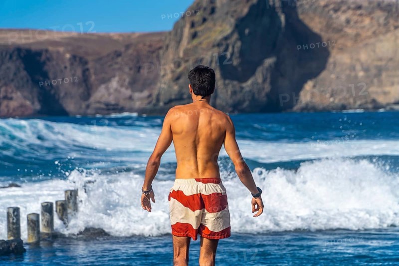 Tourist admiring the ocean waves in the natural pools of agaete, a charming coastal town in gran canaria, canary islands, spain