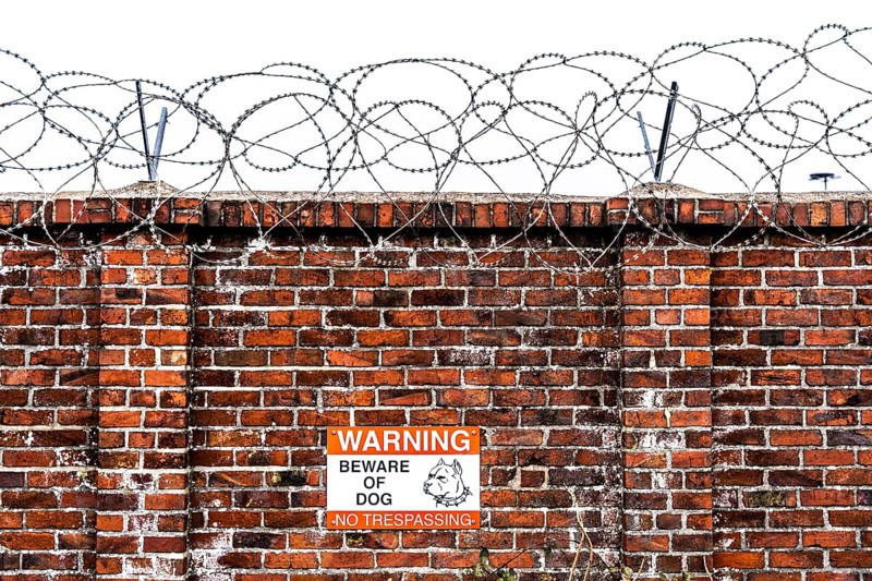 Company premises, wall secured with rolls of barbed wire, signpost for guard dog on the premises