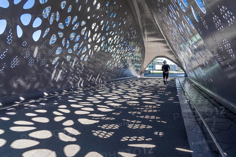 Light effects from the sun in the Parkbruk, a cycle and pedestrian bridge in the city centre of Antwerp, spanning a multi-lane city centre road with tram lines, and thus connecting two lively city districts Kop Spoor Noord and Eilandje, Belgium, without any crossings, Europe