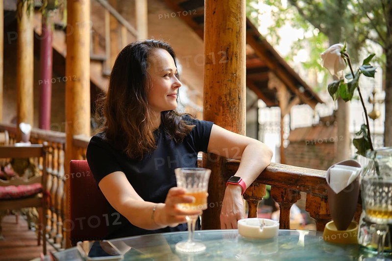 Cheerful and relaxed woman drinking white wine at rustic outdoor cafe enjoying tranquil ambiance of cozy cafe