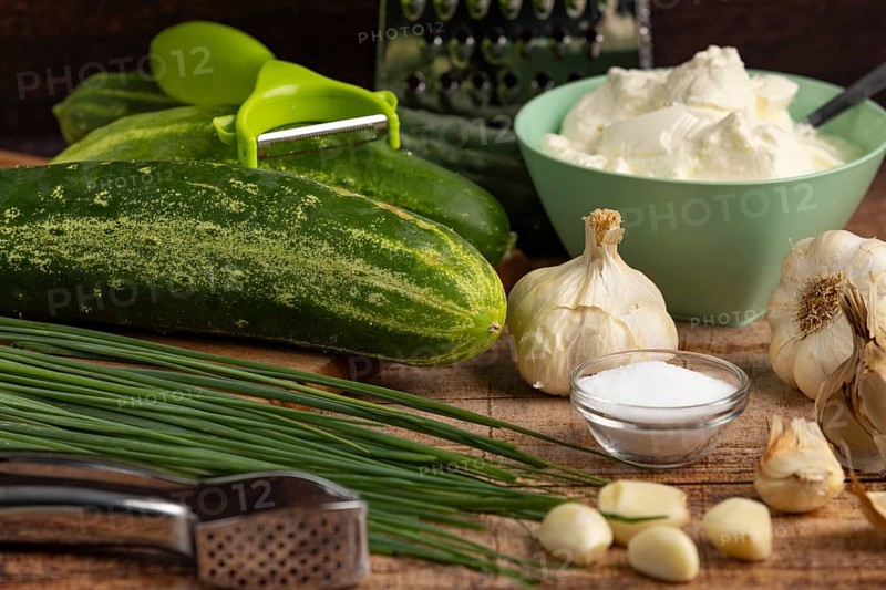 Fresh ingredients such as cucumbers, garlic, chives and sour cream on a wooden table with kitchen utensils