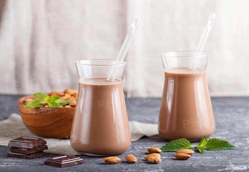 Organic non dairy almond chocolate milk in glass and wooden plate with almond nuts on a black concrete background. Vegan healthy food concept, close up, side view