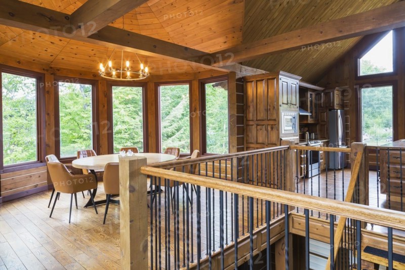Staircase, round wooden dining table with tan leather armchairs in dining room, plus kitchen inside a milled Eastern white pine timber and flat log profile home, Quebec, Canada, North America