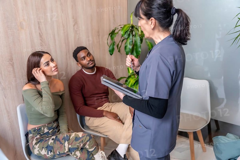 Nurse holding tablet and explaining treatment to young couple in waiting room of dental clinic