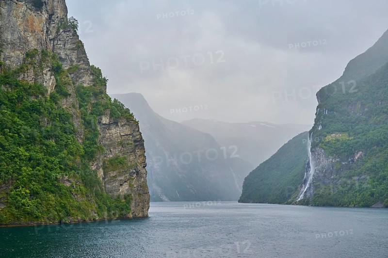 Geiranger Fjord with waterfall surrounded by rocks and mountains with overcast sky, Geiranger, Geiranger Fjord, Stranda, Romsdal, Norway, Europe
