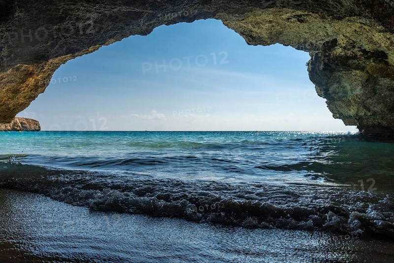 Turquoise waves gently washing onto the shore of cala domingos beach in mallorca, spain, viewed from the inside of a cave, creating a tranquil and serene scene