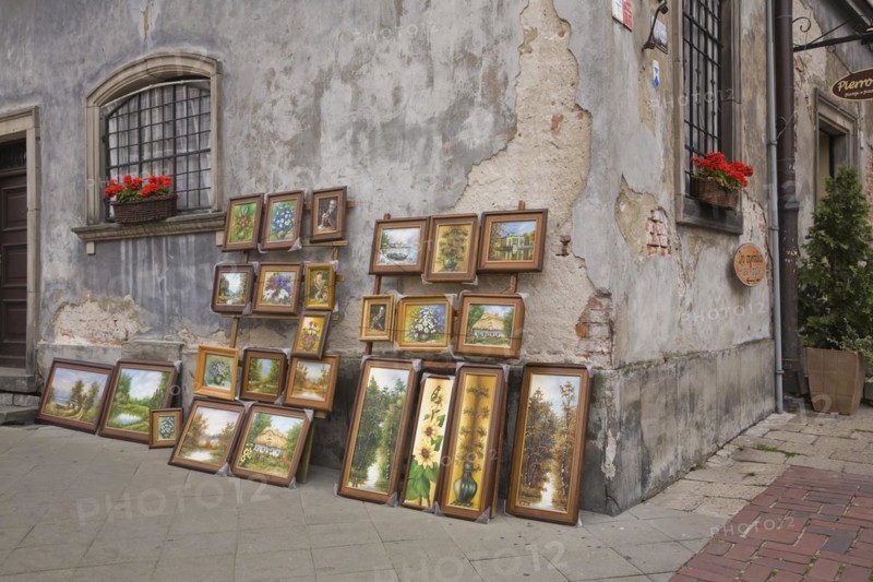 Framed paintings displayed against an old damaged grey cement wall in the Old Town Market Square, Warsaw, Poland, Europe
