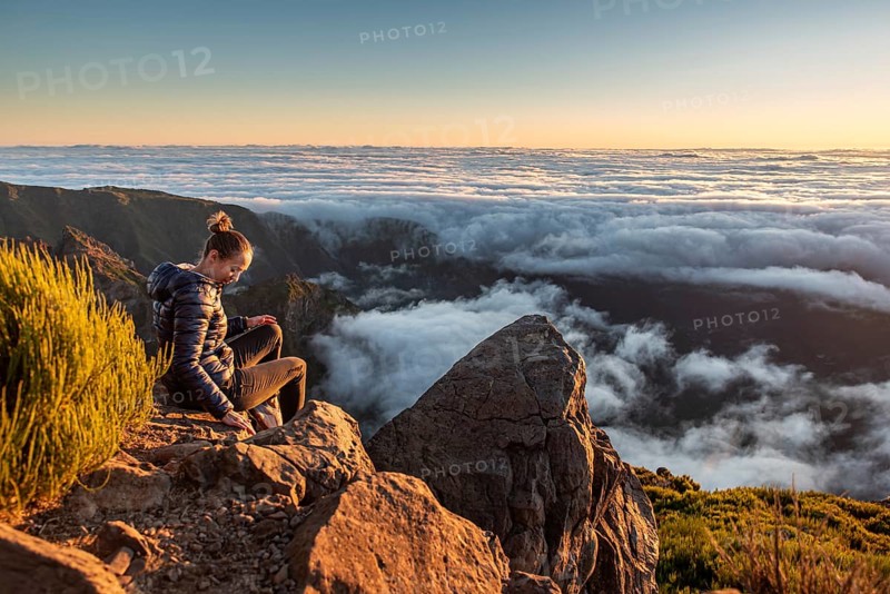 A woman sits on a rock and looks at the sea of clouds below her at dusk, Pico Ruivo, Madeira, Portugal, Europe