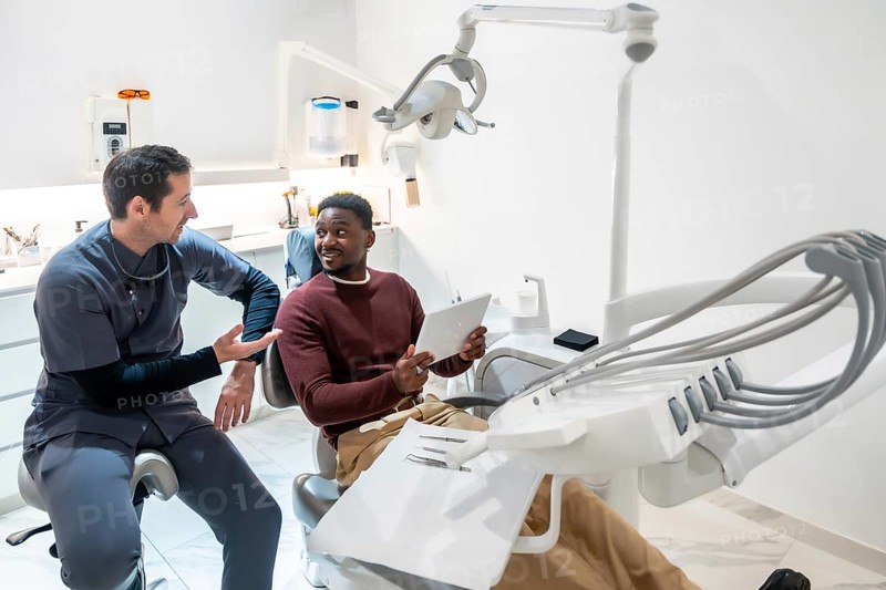 Dentist discussing treatment plan with patient using digital tablet in modern dental clinic, showcasing advanced technology and patient care