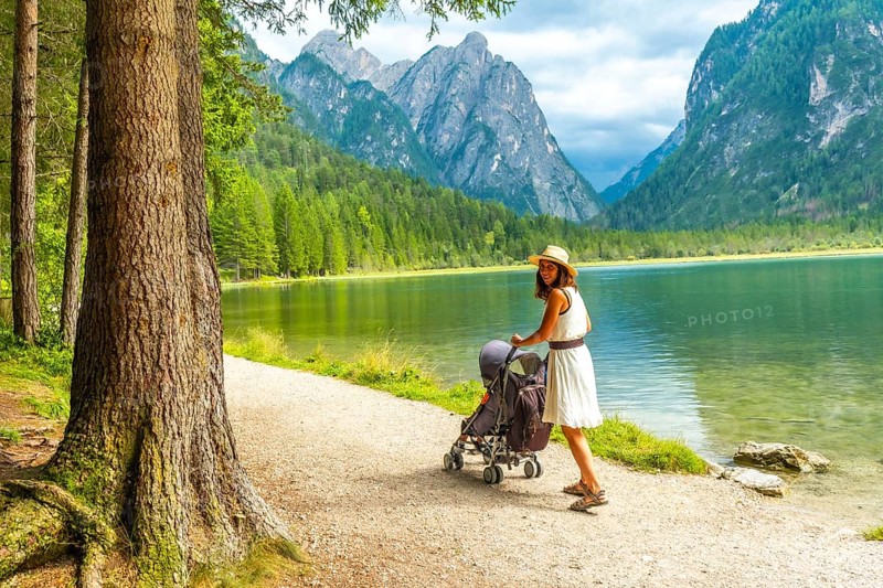 Tourist walking with stroller along lake in breathtaking mountain scenery of dolomites, italy, enjoying summer holiday