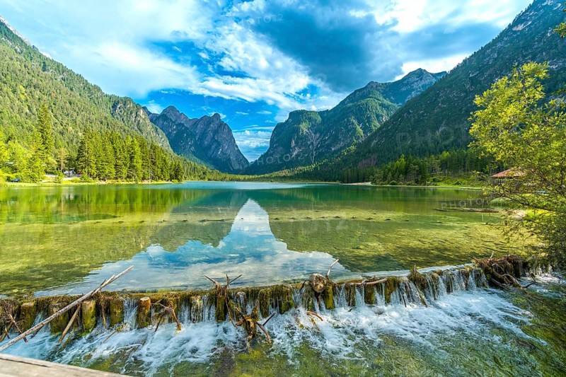 Crystal clear water flowing from lake dobbiaco, surrounded by majestic dolomites peaks, on a sunny summer day in italy