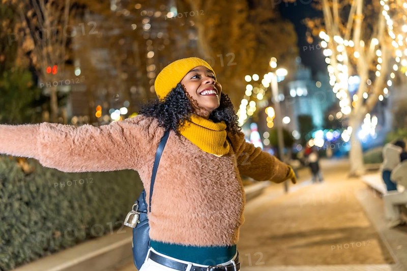 Young woman embracing the festive spirit of christmas lights while enjoying a winter evening in the city, radiating joy and happiness